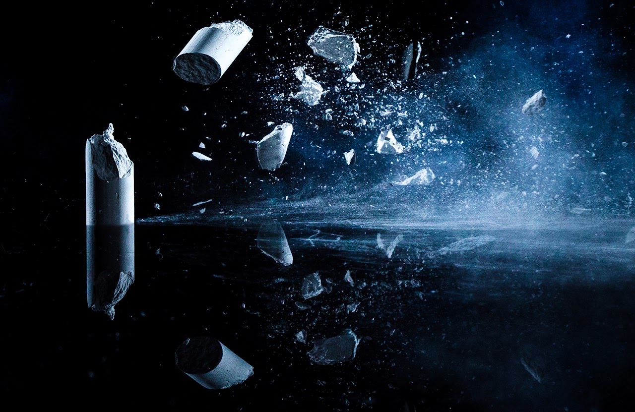 Chalk fragments exploding in a blue-lit field.
