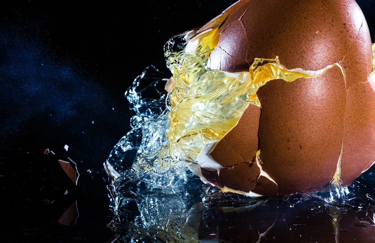Egg cracking and splashing against a black background.