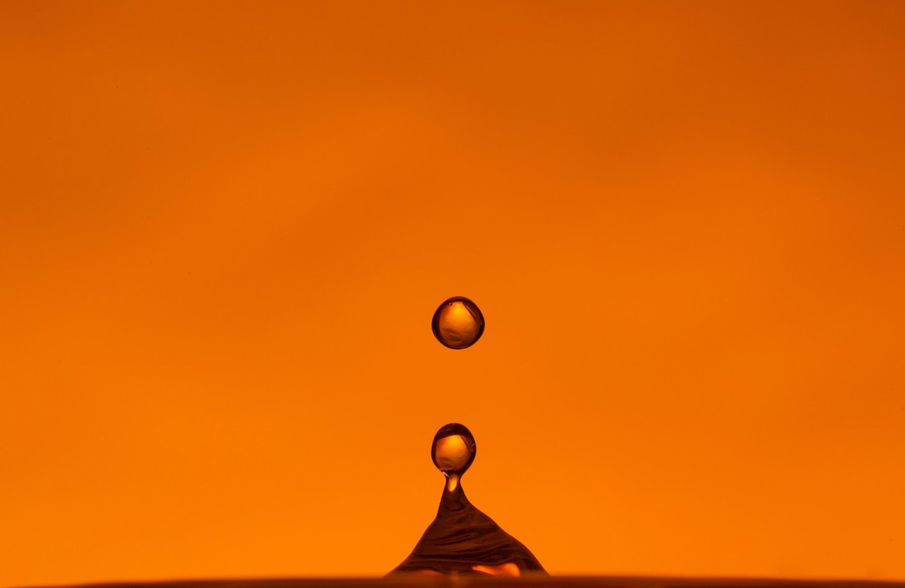 An orange water droplet suspended over a liquid peak.