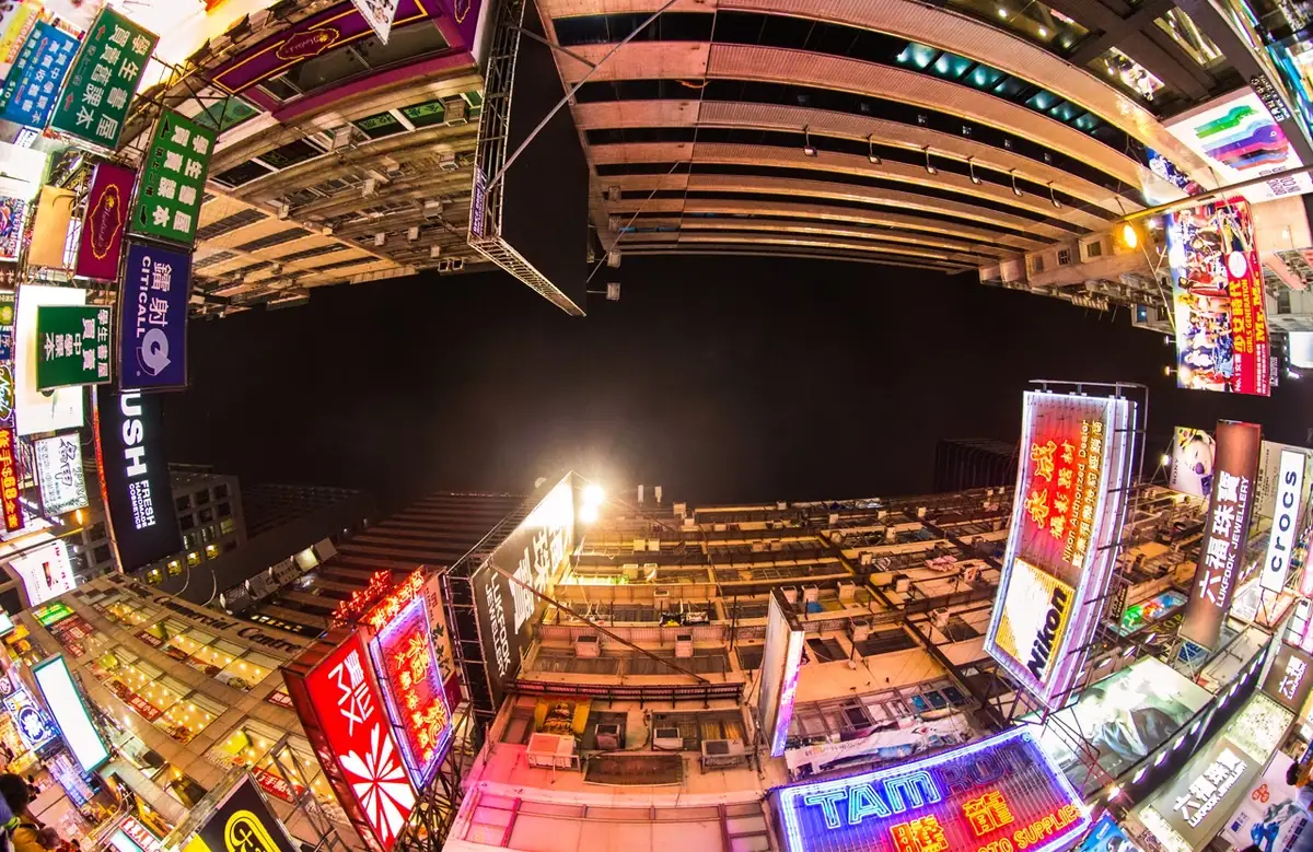 Fisheye view of Hong Kong neon signs and buildings surrounding a dark sky.