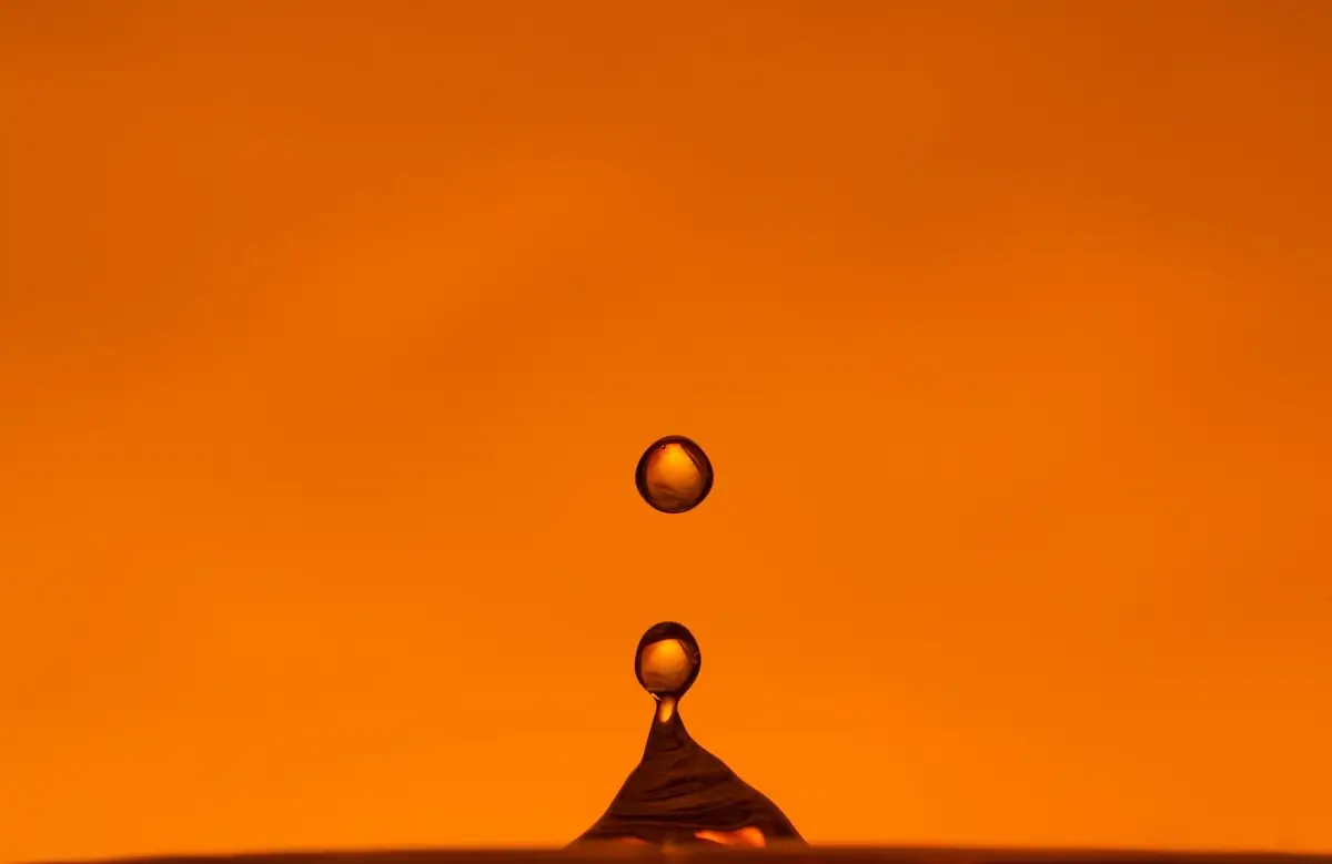 An orange water droplet suspended over a liquid peak.