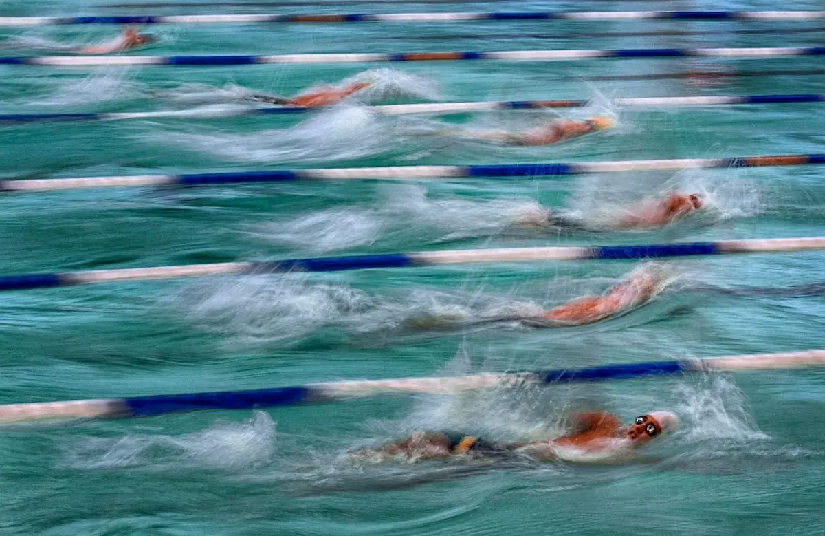 Multiple swimmers blurred into painterly strokes across a pool.