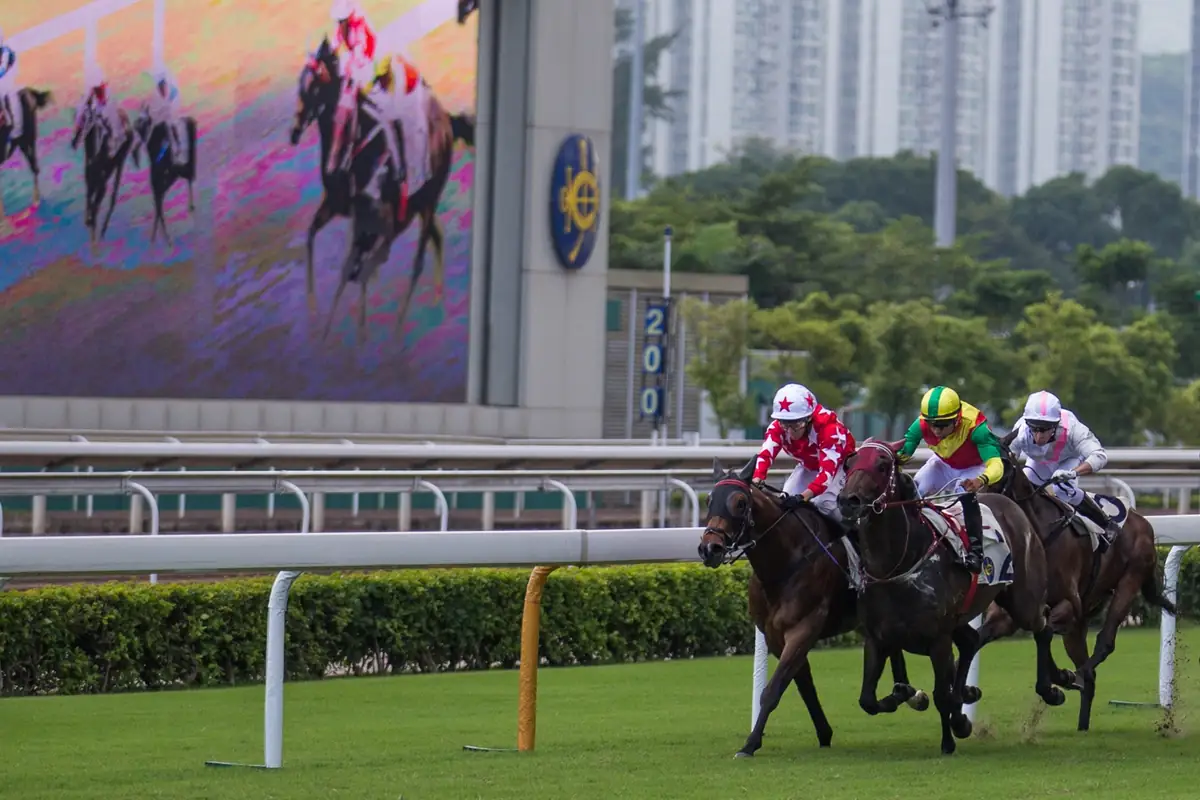 Racehorses passing below a large screen at a Hong Kong racecourse.