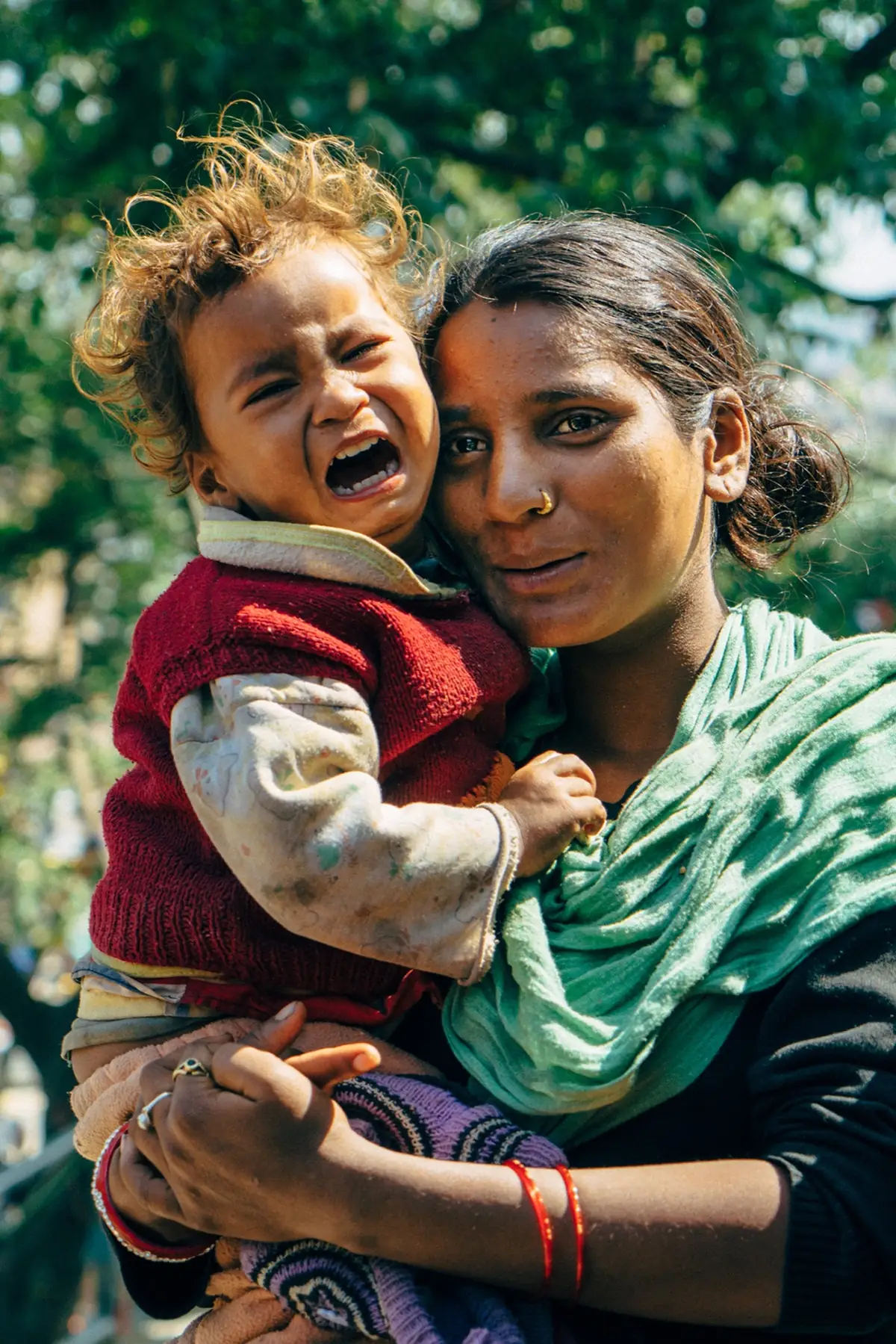 Mother holding a crying child outdoors.