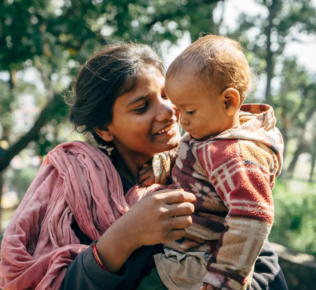 Woman holding a child close outdoors.