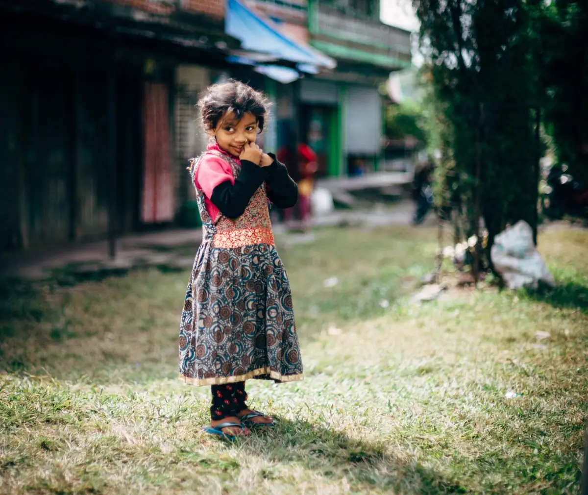 Child standing in an open yard near buildings.