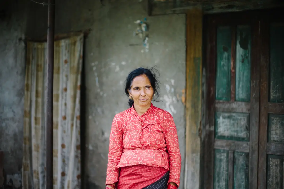 Woman seated against a weathered wall.