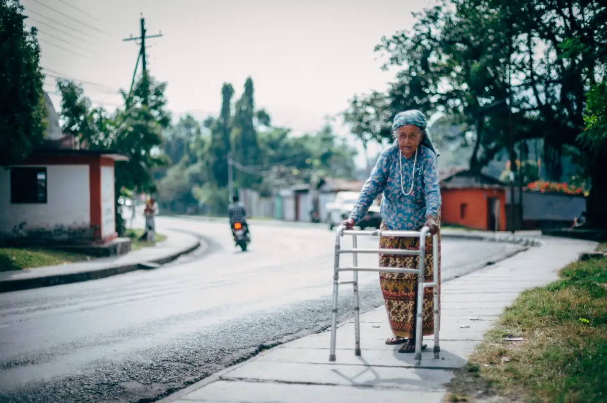 Elderly person using a walker on a road.