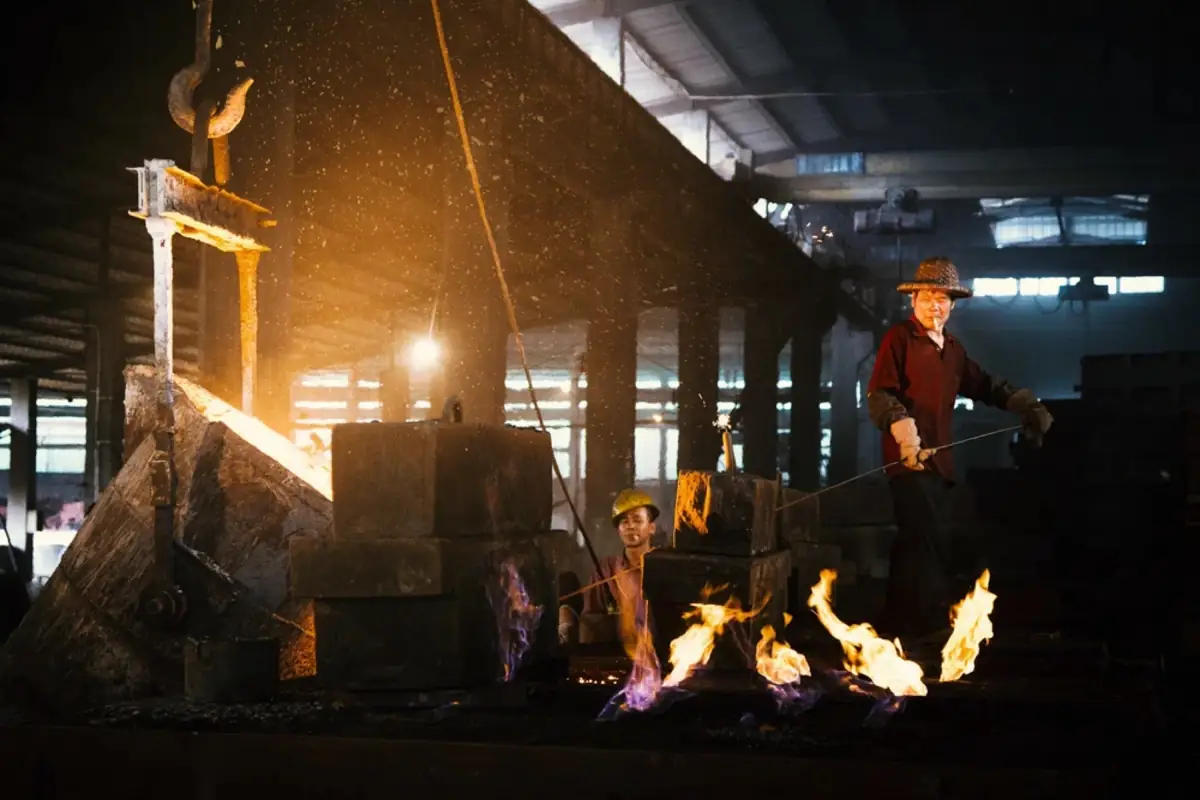 Workers and fire inside a dark industrial foundry.