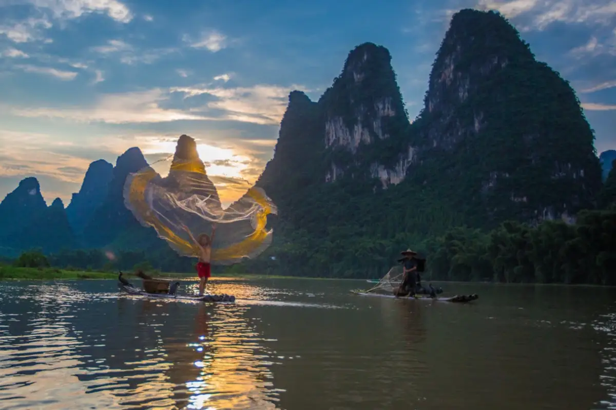 Boats on a river at dusk with karst mountains.